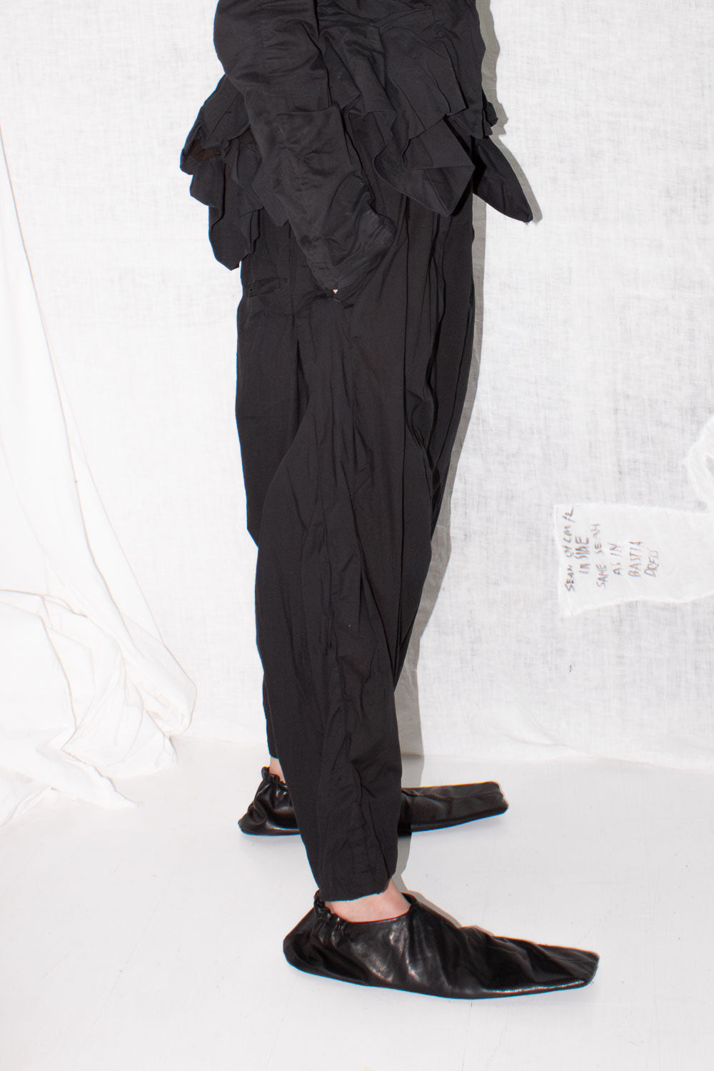 Side view of pleated trousers showing gathered waistband and multiple pleat construction details