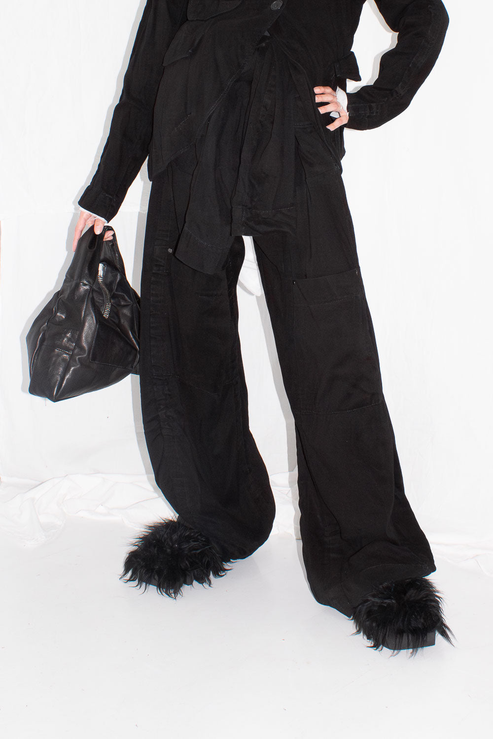 Model wearing trousers styled with black bag, showing full wide-leg proportions and fuzzy slippers