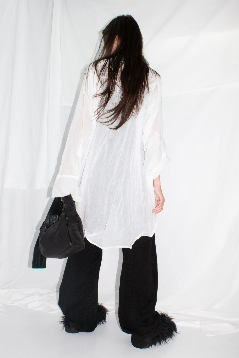 Model wearing white shirt from behind styled with black wide-leg trousers and fur boots
