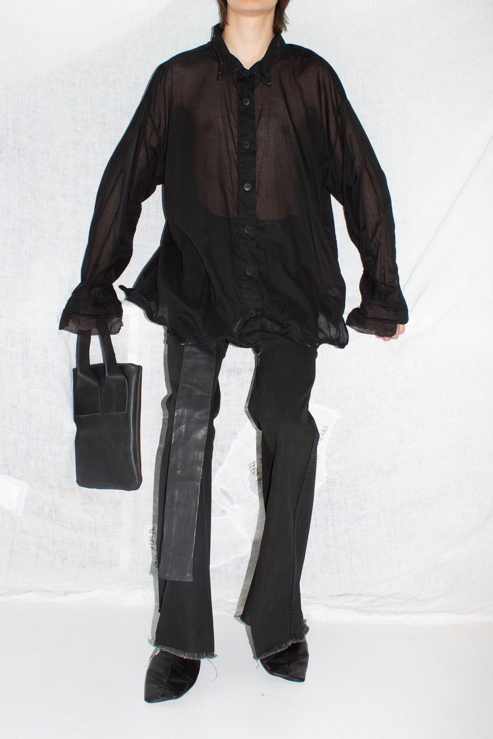 Model wearing black sheer shirt with leather trousers and structured bag in full styling