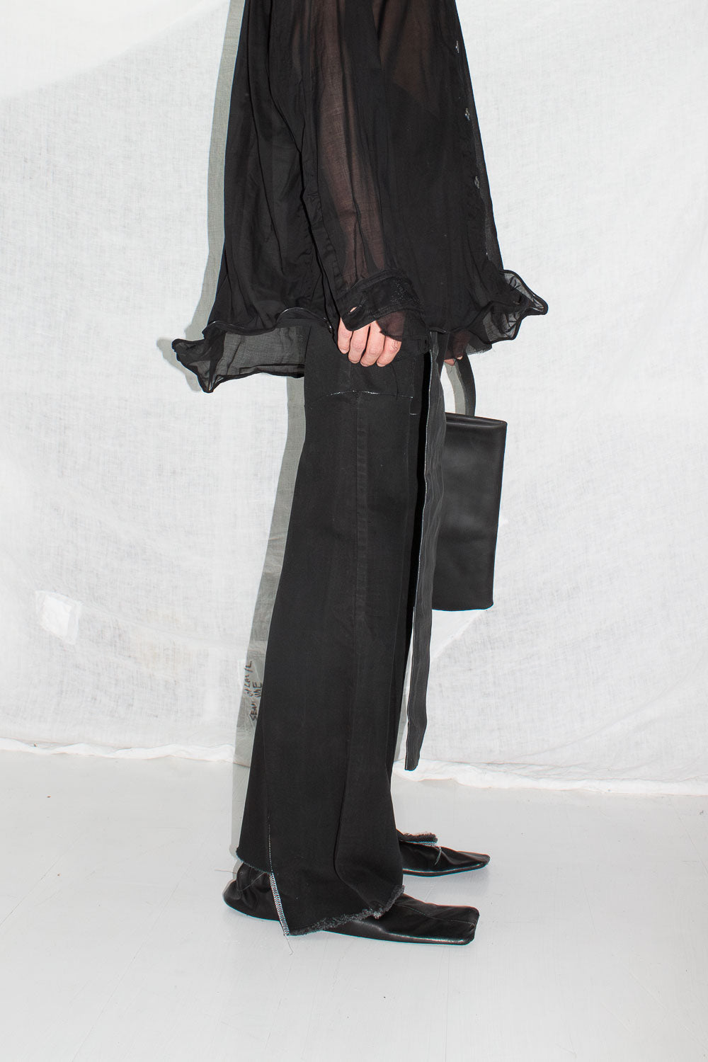Detail of black sheer shirt worn with black trousers and geometric bag, showing length and drape