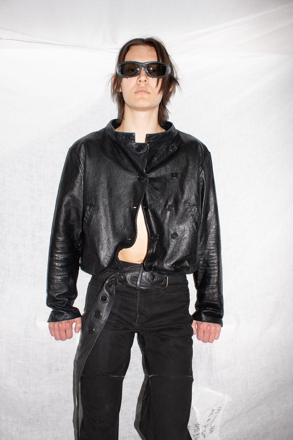 Front view of model in black leather jacket with asymmetrical buttoning and exposed midriff styling