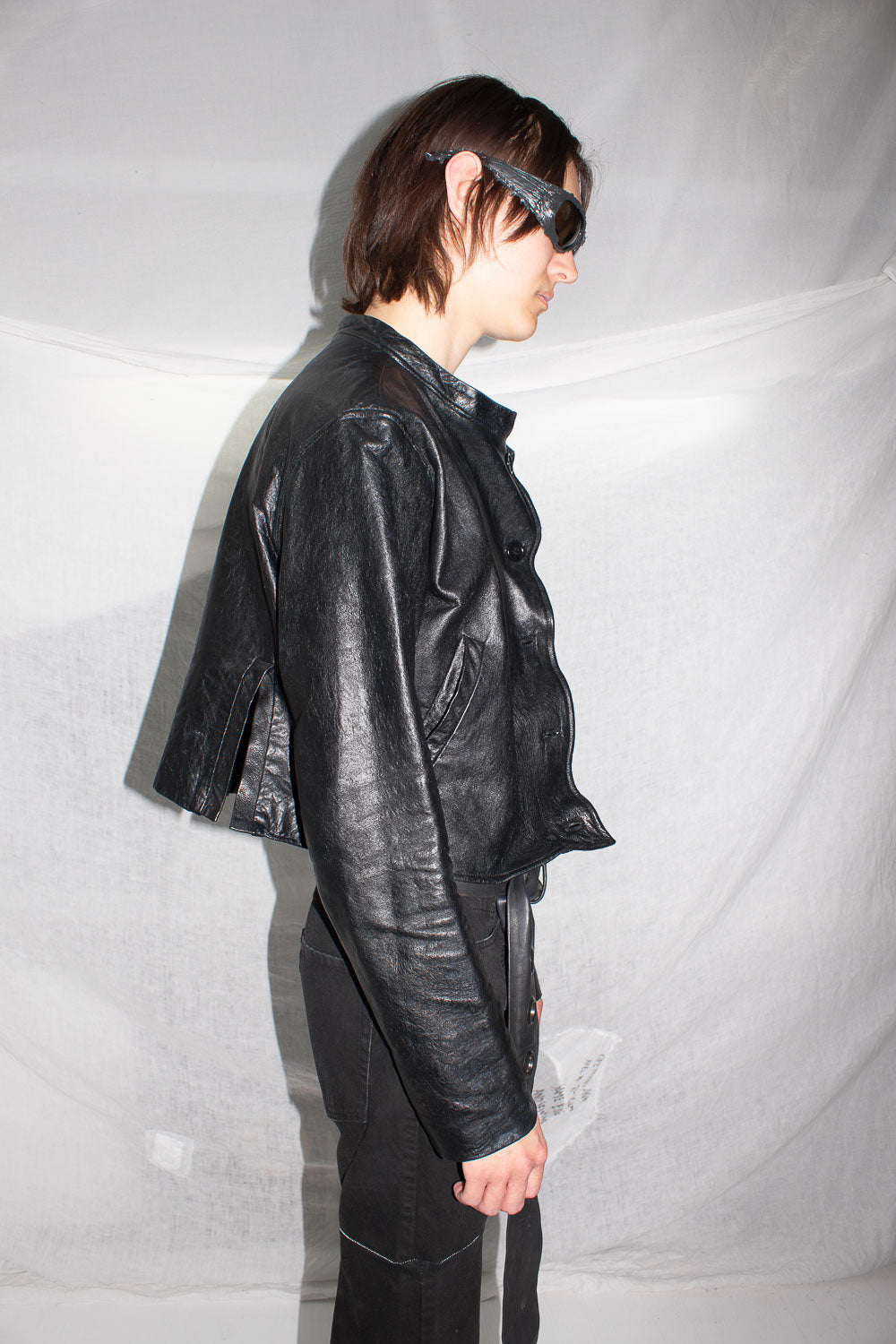 Side profile of model in black leather jacket revealing angled front construction and sculptural hem shaping