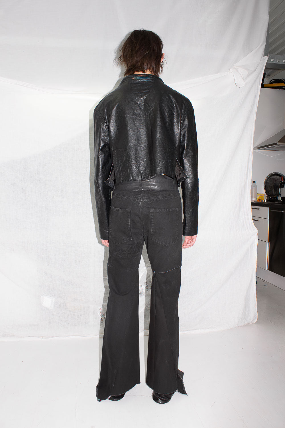 Back view of figure wearing black leather jacket and flared denim trousers