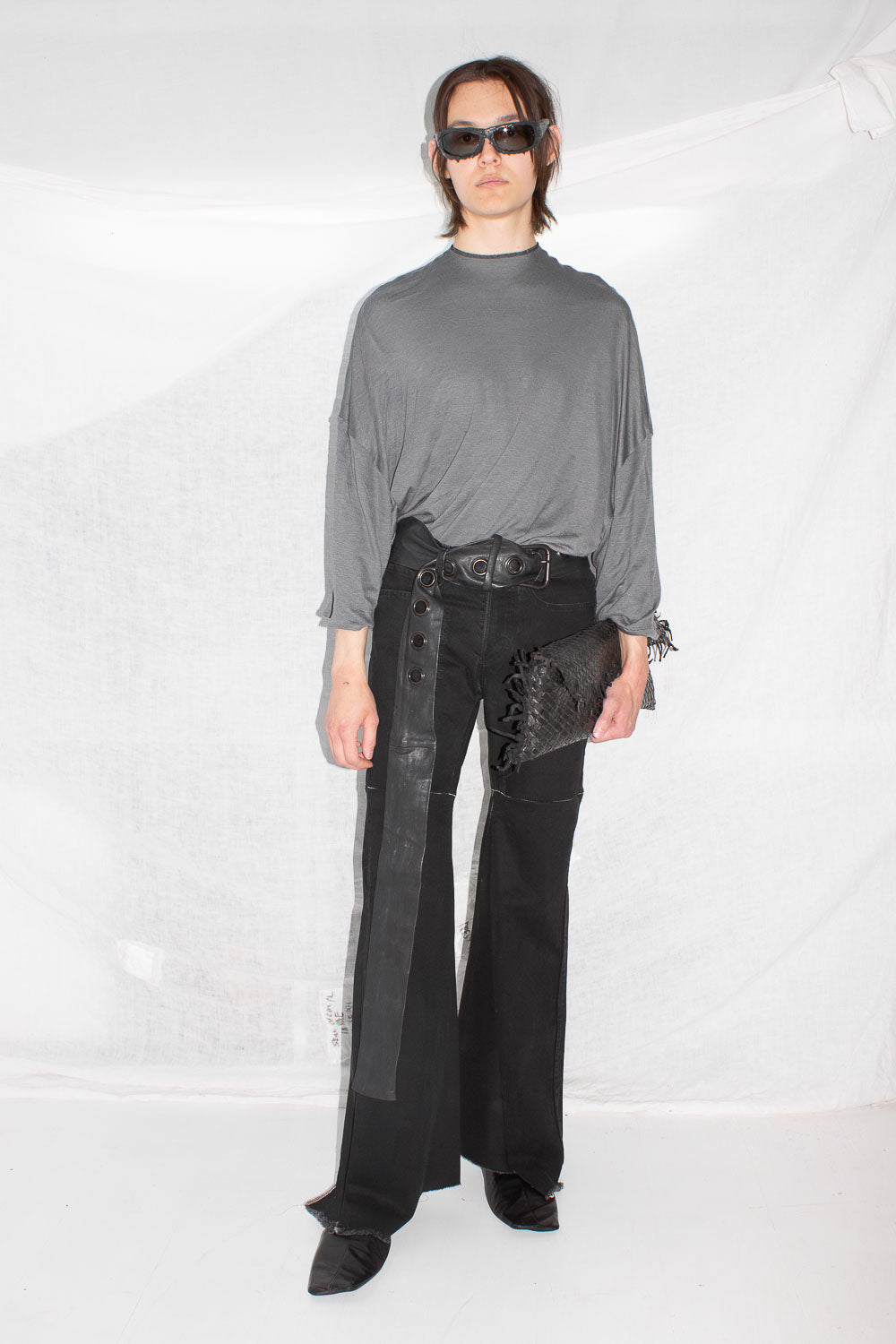 Front view of model in grey t-shirt with sunglasses, styled with leather pants and clutch