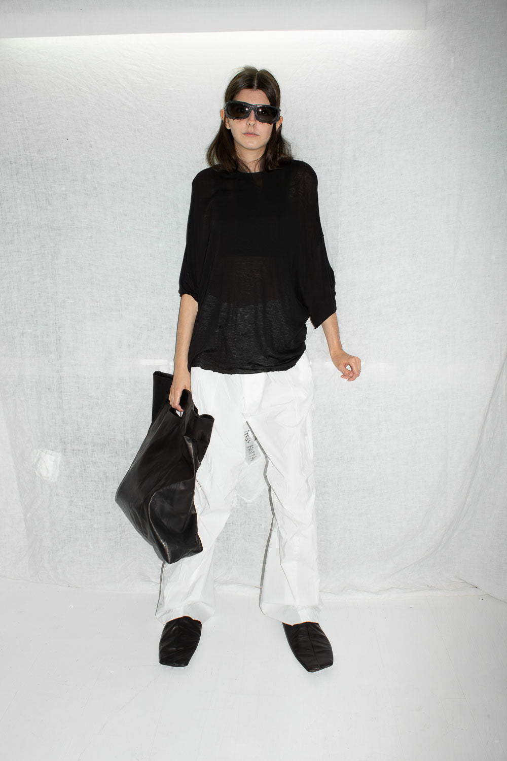Full body shot of model in black oversized t-shirt with white wide-leg trousers and leather bag