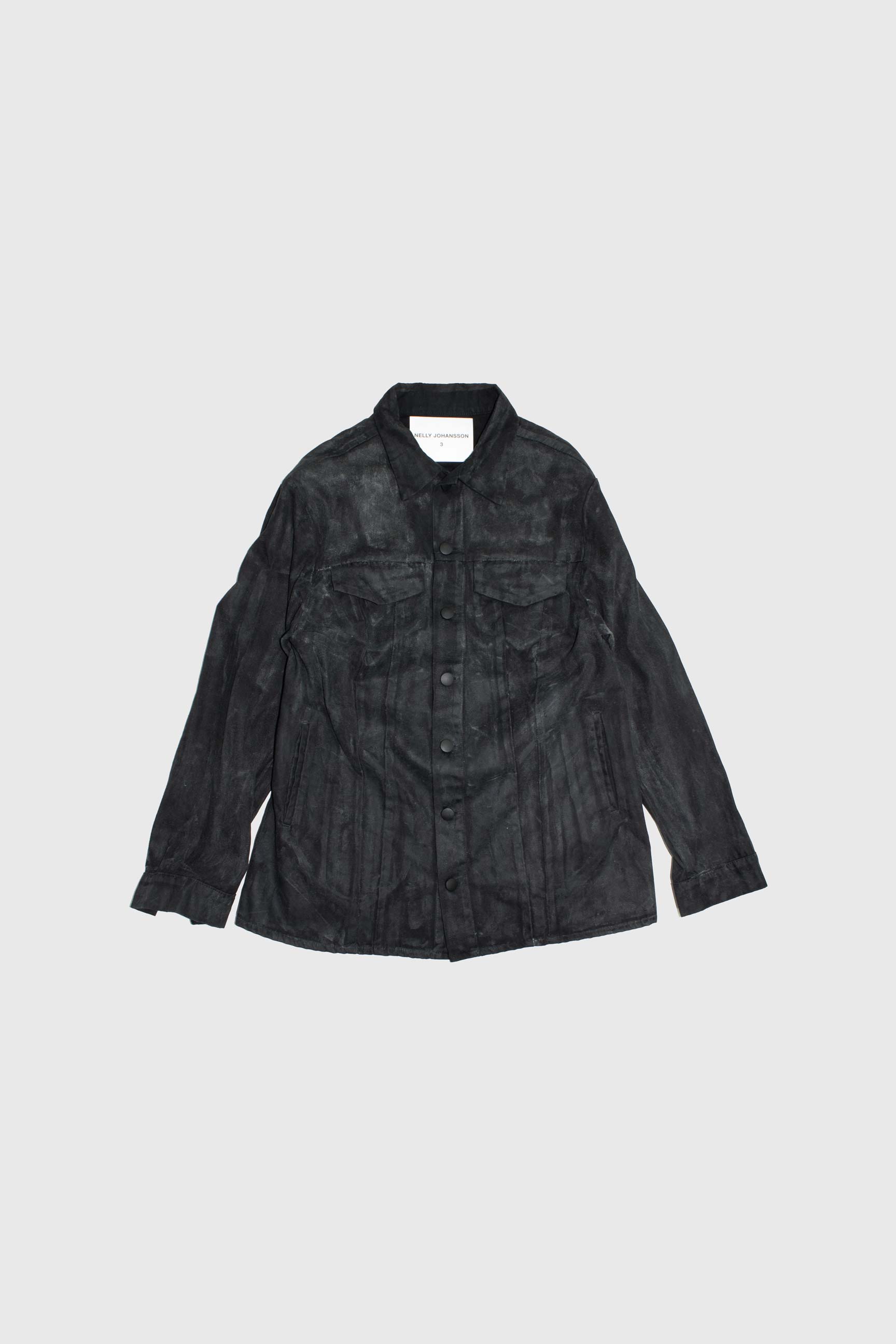 Black waxed denim jacket with chest pockets and snap closures laid flat on light background