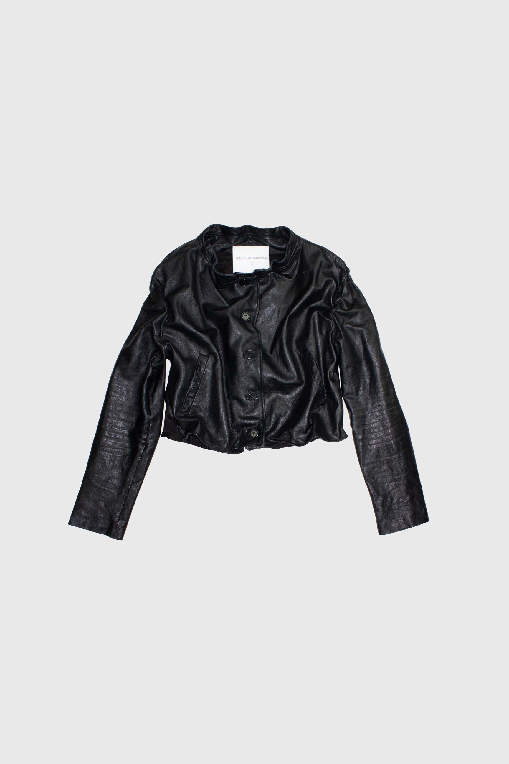 Black leather cropped jacket flat lay showing double-breasted button closure and sculptural wire-framed hem detail