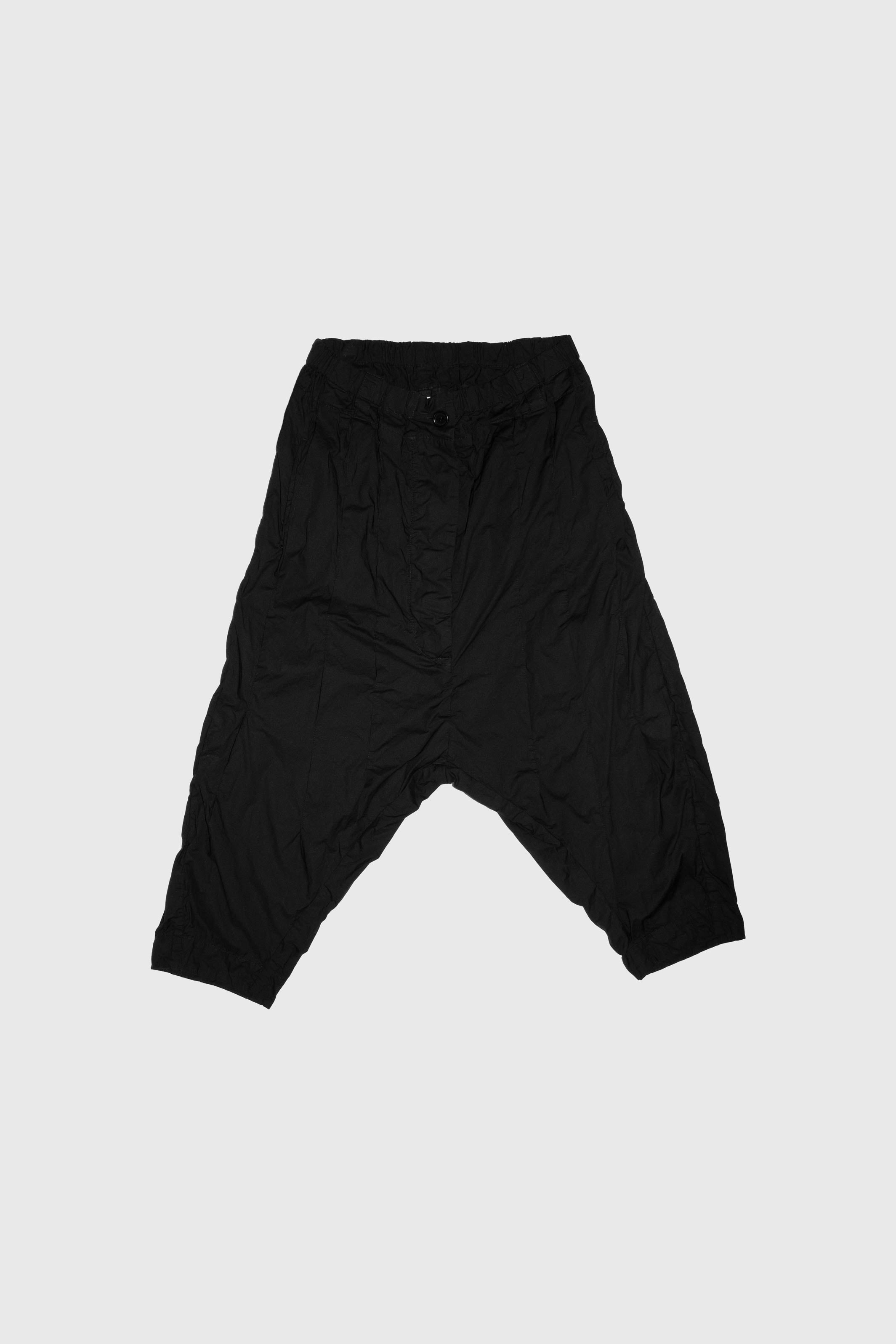 Flat lay of black pleated trousers showing dropped crotch construction and pleated detailing